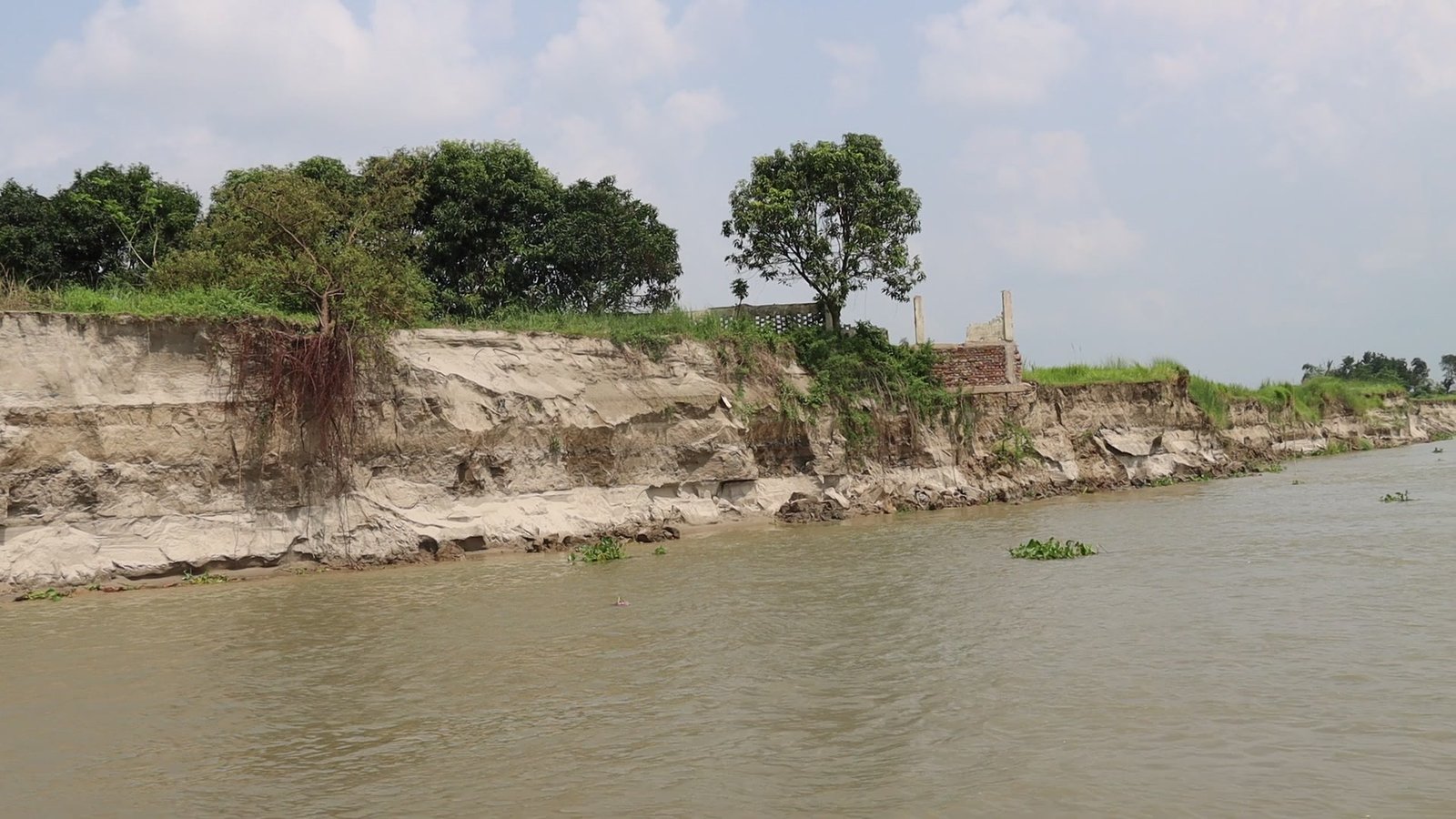 A long stretch of riverbank cut away by the current, trees and a broken brick wall left standing at the edge