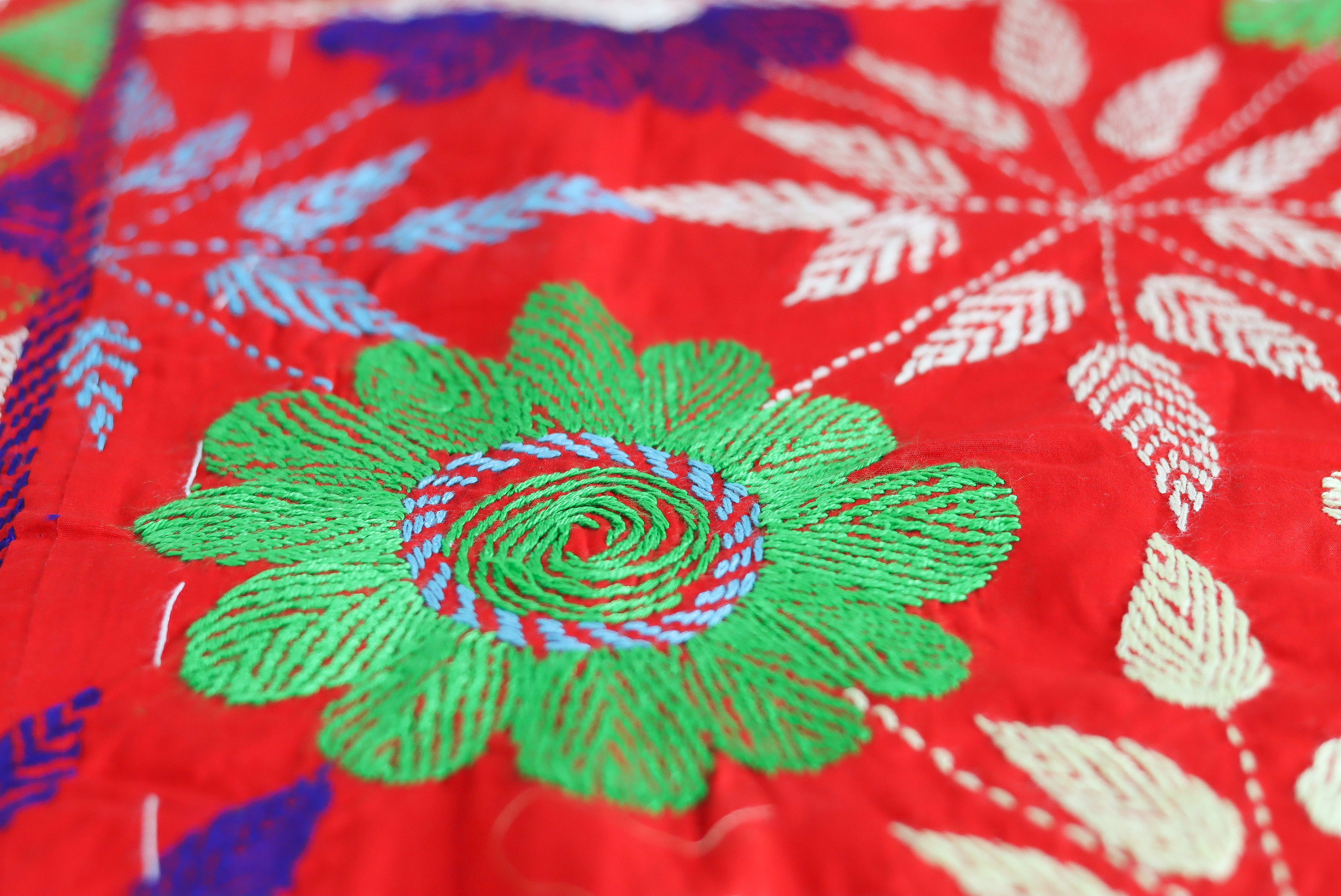An artisan embroidering a kantha hoop by a plant-filled workshop window